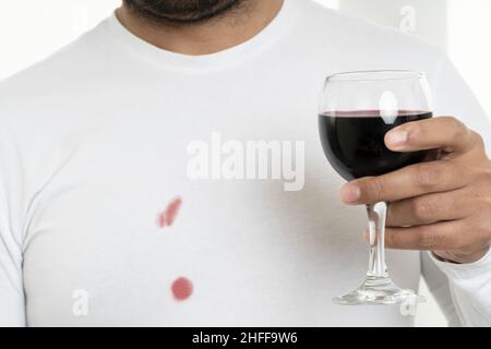 Nahaufnahme eines Mannes, der Weinglas hält und ein weißes Hemd trägt. Konzept der Wäsche und Waschen schmutziger Kleidung. Stockfoto