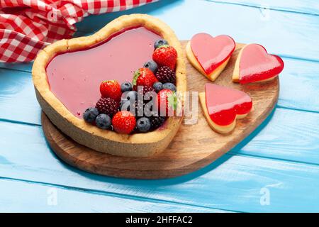 Herzförmiger süßer Kuchen mit Beeren und Keksen. Grußkarte zum Valentinstag Stockfoto