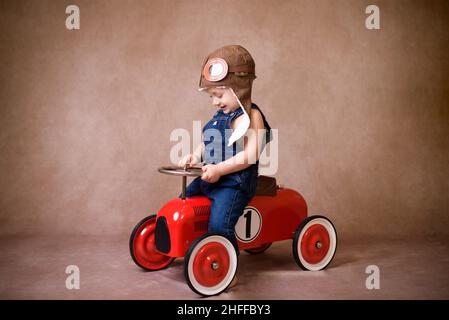 Lustige niedliche Kind in roter Jacke fahren großen alten Spielzeugauto und Spaß, im Freien. Kinder können sich an kalten Tagen im Winter, Herbst oder Frühling entspannen Stockfoto