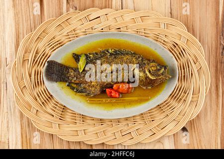 Pesmol Ika Nila, Tilapia Gelbe Curry, beliebtes Curry Rezept aus gebratenen Fischen in West-Java, Indonesien. Isoliert. Holzhintergrund Stockfoto