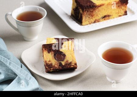 Köstliche hausgemachte Marmorkuchenscheiben auf cremefarbenem Hintergrund, serviert mit Tee Stockfoto