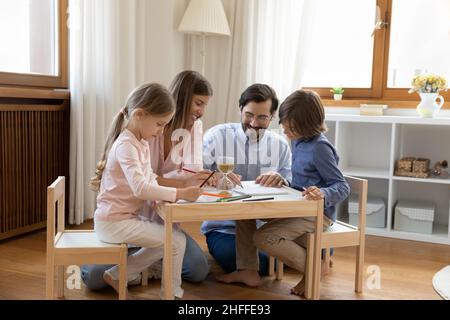 Junge Eltern und Kinder, die sich zusammenziehen, sitzen in einem modernen Kinderzimmer Stockfoto