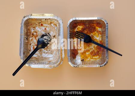 Zwei leere Aluminiumbehälter nach dem Mittagessen von oben. Lebensmittelbehälter mit Einweg-Plastikutensilien. Schmutziges Einweggeschirr nach dem Essen auf einer Be Stockfoto