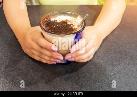 Weibliche Hände mit lackierten Nägeln, die ein Glas Latte Macchiato Kaffee mit Schokolade halten Stockfoto