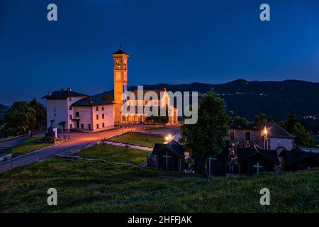 Die hiesige Kirche von Fuipiano Chiesa di San Giovanni Battista leuchtet nachts, die umliegenden Hügel in der Ferne. Stockfoto