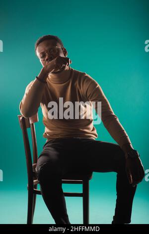Schöner und feingepasster schwarzer Mann posiert toll auf dem Stuhl im Studio Stockfoto