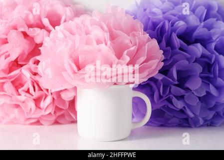 Weißer Mockup-Becher auf einem rosa Papierblumen-Hintergrund. Stockfoto