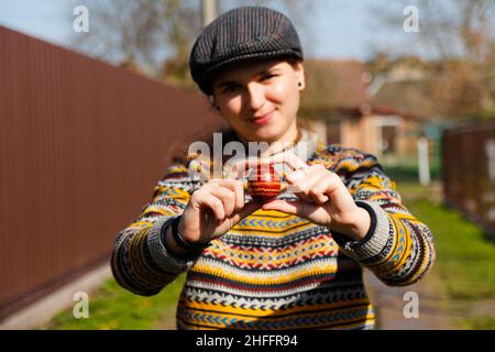 Fröhliche lächelnde Frau mit einem farbigen roten Ei, Osterfeiertagskonzept. Hände mit modernen bemalten ostereiern. Junge Hipster Millennial Frau in Stockfoto