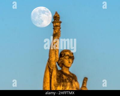 Sheerness, Kent, Großbritannien. 16th Januar 2022. Wetter in Großbritannien: Der fast volle Wolf Moon erhebt sich heute Nachmittag hinter der Freiheitskriegs-Gedenkstatue in Sheerness, Kent. Kredit: James Bell/Alamy Live Nachrichten Stockfoto