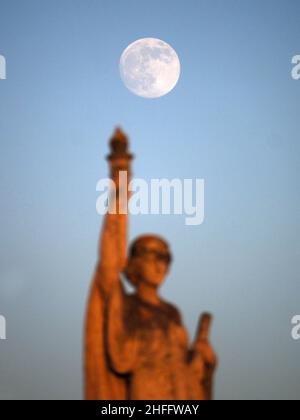 Sheerness, Kent, Großbritannien. 16th Januar 2022. Wetter in Großbritannien: Der fast volle Wolf Moon erhebt sich heute Nachmittag hinter der Freiheitskriegs-Gedenkstatue in Sheerness, Kent. Kredit: James Bell/Alamy Live Nachrichten Stockfoto