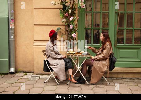 Lviv, Ukraine - 26.09.2021: Zwei junge Frauen trinken draußen im Hintergrund der Altstadt Tee oder Kaffee. Menschen, Kommunikation und Freundschaft Konzept: Frauen Stockfoto