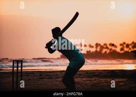 Silhouette von Jungen, die am Meer Cricket spielen Stockfoto