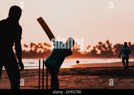 Silhouette von Jungen, die am Meer Cricket spielen Stockfoto