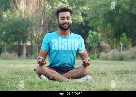 Attraktive asiatische Mann sitzt in Meditation Pose Position Yoga Pranayama Gleichgewicht in der schönen Blick auf den Park während des Sonnenuntergangs. Gesundheit und Wellness Stockfoto