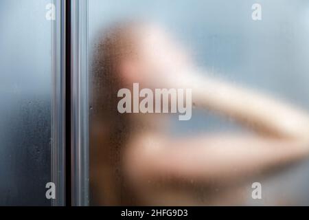 Rückansicht einer Frau, die im Badezimmer duscht. Verschwommenes Bild. Stockfoto