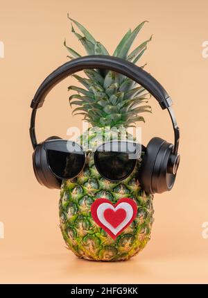 Die Idee von Liebhabern zum valentinstag im Bild einer Ananas mit Kopfhörern und Sonnenbrillen. Auf gelbem Hintergrund. Stockfoto