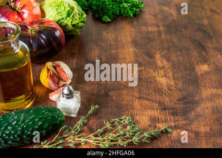 Holzhintergrund in abgenutzter brauner Farbe, auf einer Seite mit Gemüse, Öl, Salz und Pfeffer. Stockfoto