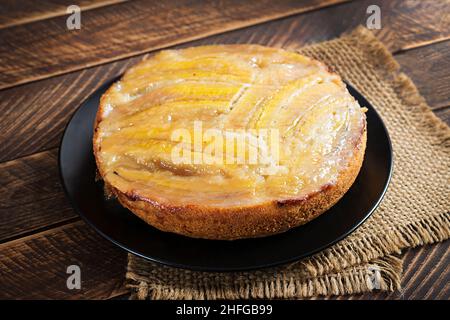 Bananenkaramellkuchen oder Kuchen auf einem schwarzen Teller auf einem Holzhintergrund. Stockfoto