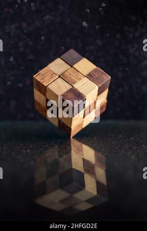 rubiks Würfel aus Holz steht im Gleichgewicht am Rand auf einem reflektierenden schwarzen Glas Stockfoto