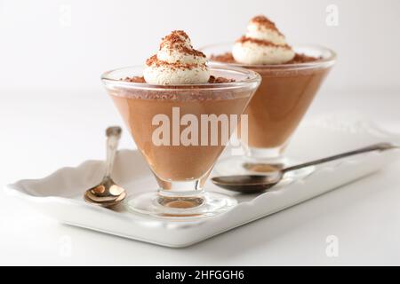 Schokoladen-Mousse-Desserts in konischen Glastellern auf einem Serviertablett aus weißem Porzellan mit Löffeln, garniert mit Creme und geriebener dunkler Schokolade Stockfoto