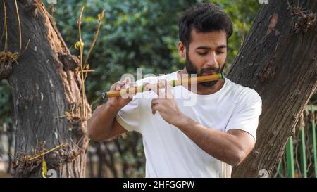 Bansuri-Spieler, der bei Sonnenschein im Park Musik spielt - Indian Flute Player Stockfoto