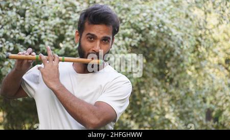 Bansuri-Spieler, der bei Sonnenschein im Park Musik spielt - Indian Flute Player Stockfoto