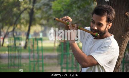 Bansuri-Spieler, der bei Sonnenschein im Park Musik spielt - Indian Flute Player Stockfoto