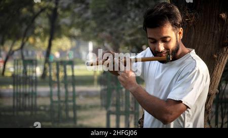 Bansuri-Spieler, der bei Sonnenschein im Park Musik spielt - Indian Flute Player Stockfoto