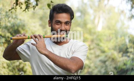 Bansuri-Spieler, der bei Sonnenschein im Park Musik spielt - Indian Flute Player Stockfoto