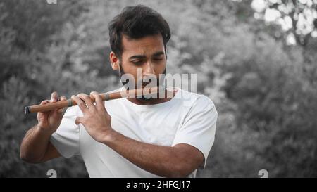 Bansuri-Spieler, der bei Sonnenschein im Park Musik spielt - Indian Flute Player Stockfoto