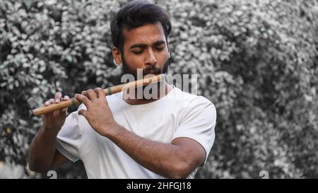 Bansuri-Spieler, der bei Sonnenschein im Park Musik spielt - Indian Flute Player Stockfoto