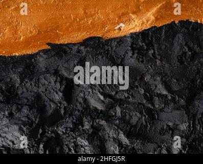 Volumetrischer Hintergrund der Wand mit schwarz aus Gold-Kupfer oder orange Farbe lackiert. Trennung von zwei Farben. Geprägter bicolor Hintergrund Stockfoto