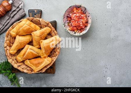 Gebratene Empanadas mit Koriander, Fleisch, Ei, Tomaten und Chilisauce auf grauem Hintergrund. Typisch chilenisches Gericht. Tag der Unabhängigkeit Lateinamerikas und Chiles Stockfoto