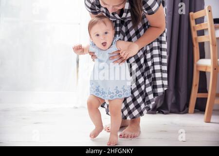 Kleinkind Mädchen lächelt und lernt mit Hilfe ihrer Mutter zu gehen Stockfoto