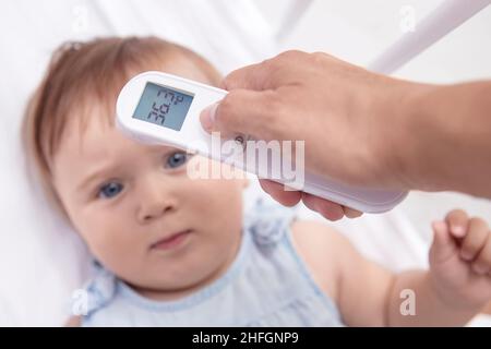 Mutter überprüft die Temperatur des Babys mit einem modernen elektronischen Termomether an der Stirn des Babys Stockfoto