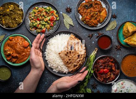 Weibliche Hände servieren ein indisches, ethnisches Buffet auf einem rustikalen Betontisch Stockfoto