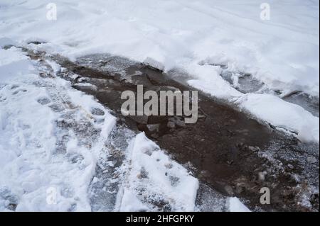 Rissige Eiskruste auf einer gefrorenen Straße. Anfang Frühling. Stockfoto