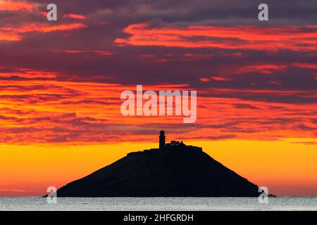 Der Sonnenaufgang am Strand von Ballynamona in der Grafschaft Cork, Irland, mit dem Leuchtturm von Ballycotton im Hintergrund Stockfoto