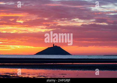 Der Sonnenaufgang am Strand von Ballynamona in der Grafschaft Cork, Irland, mit dem Leuchtturm von Ballycotton im Hintergrund Stockfoto