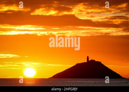 Der Sonnenaufgang am Strand von Ballynamona in der Grafschaft Cork, Irland, mit dem Leuchtturm von Ballycotton im Hintergrund Stockfoto