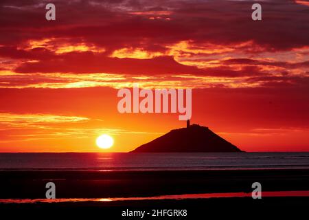 Der Sonnenaufgang am Strand von Ballynamona in der Grafschaft Cork, Irland, mit dem Leuchtturm von Ballycotton im Hintergrund Stockfoto