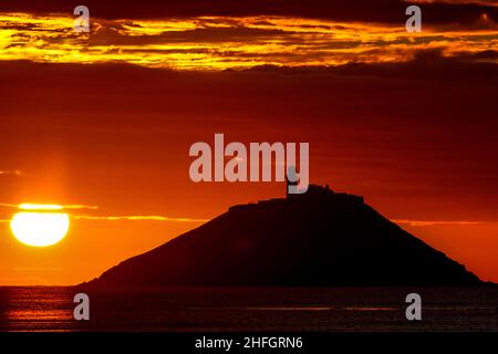 Der Sonnenaufgang am Strand von Ballynamona in der Grafschaft Cork, Irland, mit dem Leuchtturm von Ballycotton im Hintergrund Stockfoto