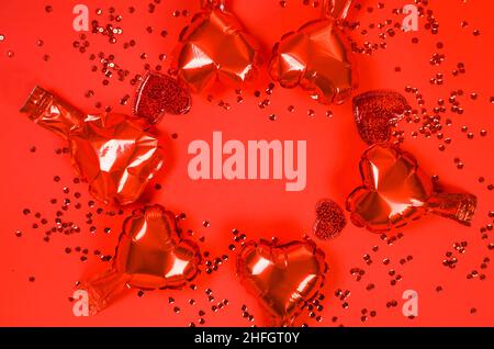 Rote Herzen Folienballons und verstreute Glitzer Draufsicht auf rotem Hintergrund für Valentinstag. Speicherplatz Kopieren. Stockfoto