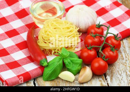 Zutaten zum Kochen von Pasta: Tagliatelle, Kirschtomaten, Knoblauch, frisches Basilikum, Chili und eine Schüssel Olivenöl Stockfoto