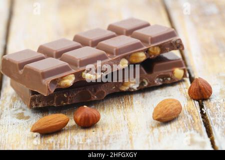 Zwei Milchschokoladenstücke mit ganzen Haselnüssen und Mandeln auf rustikaler Holzoberfläche Stockfoto