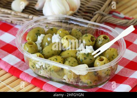 Frische grüne Oliven mit Knoblauch in transparenter Kunststoffbox auf kariertem Tuch Stockfoto
