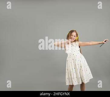 Ein schönes Mädchen in einem hellen Kleid posiert mit einem Telefon in den Händen auf einem grauen isolierten Hintergrund. Stockfoto