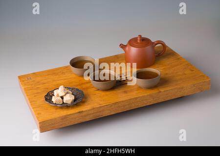 Eine Teedose und drei Tassen frisch gebrühten pu-erh-Tee, gepresster Zucker. Ein Set auf einem Holztisch für Teezeremonien. Stockfoto