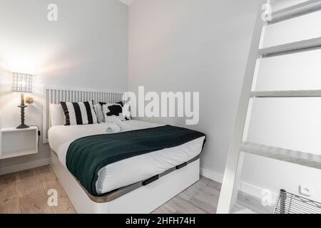 Schlafzimmer mit King-Size-Bett und Kuhkissen mit einer weißen Metalltreppe und einer hübschen Lampe in einem kurzfristigen Mietapartment Stockfoto