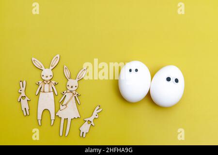 Familie von lustigen Hasen aus Sperrholz sind auf dem gelben Hintergrund geschnitten. Eine fröhliche weiße Eier mit Augen. Kreatives Bild. Design der „Easter Concept Card“. C Stockfoto